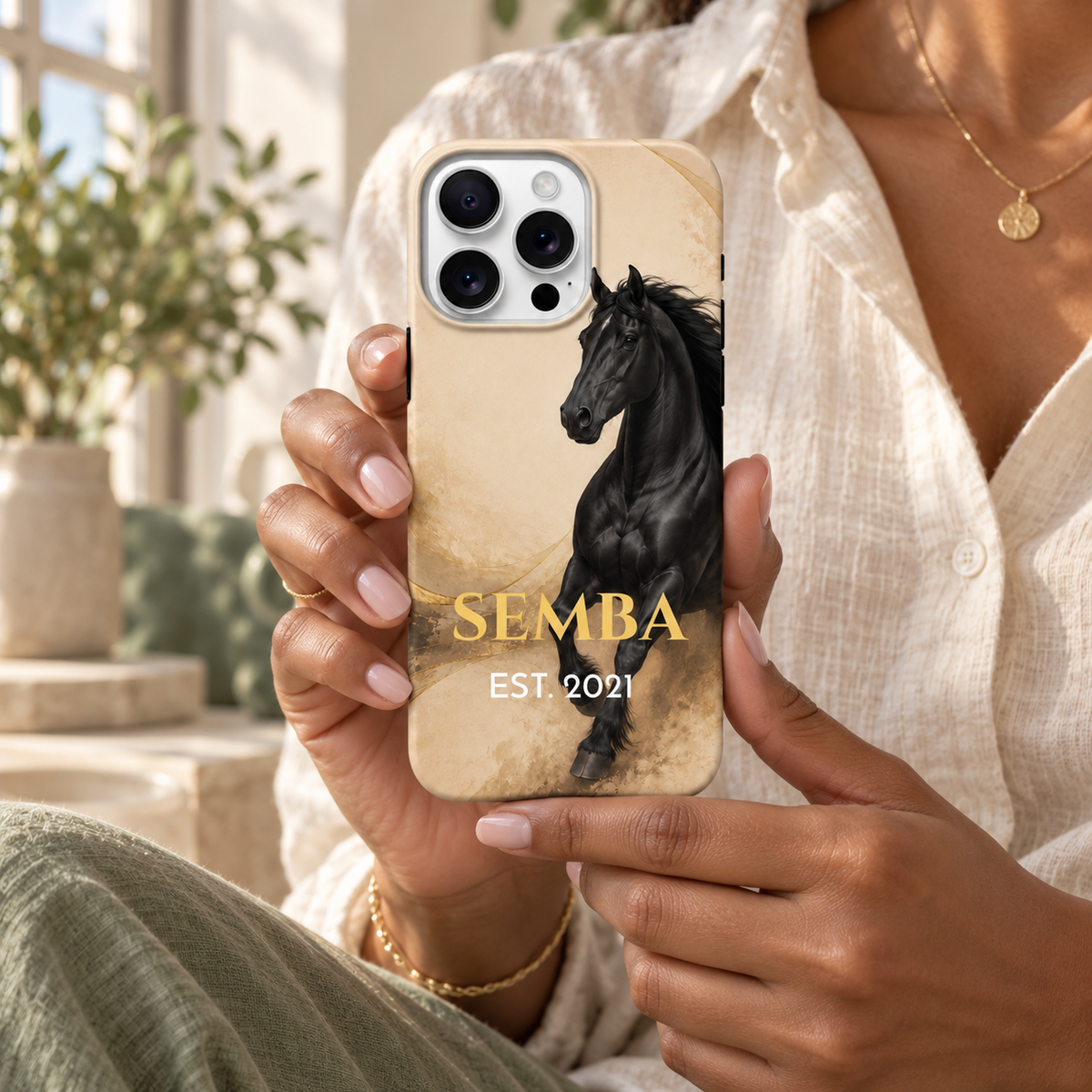 Coque personnalisée SEMBA au cheval noir sur fond crème et doré, tenue en main.