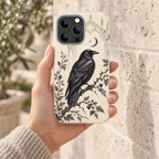 Coque Corbeau & Lune, motif ivoire, tenue en main devant un mur de pierre claire.