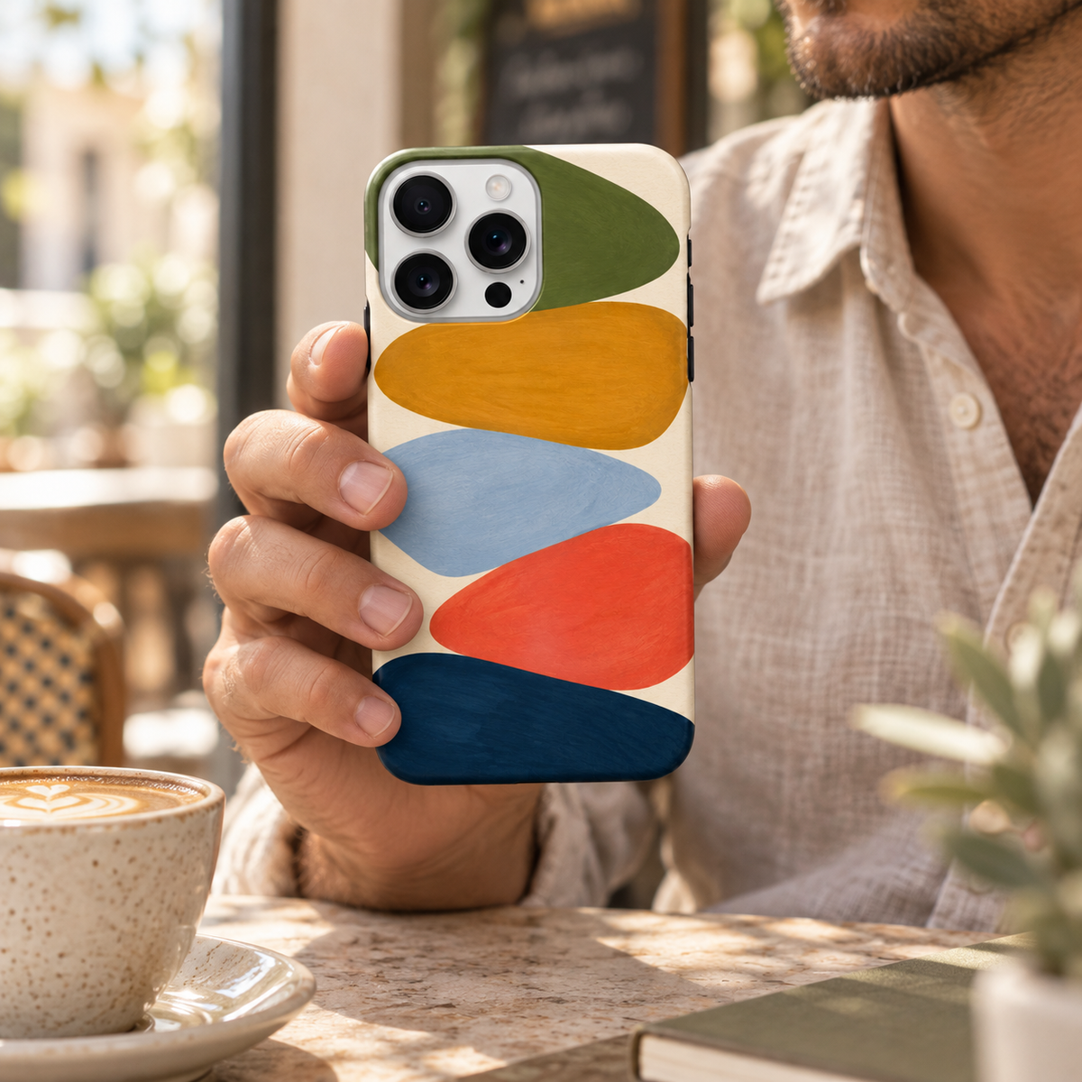 Coque Géométrie en couleurs tenue en main dans un café, avec son motif abstrait imprimé.
