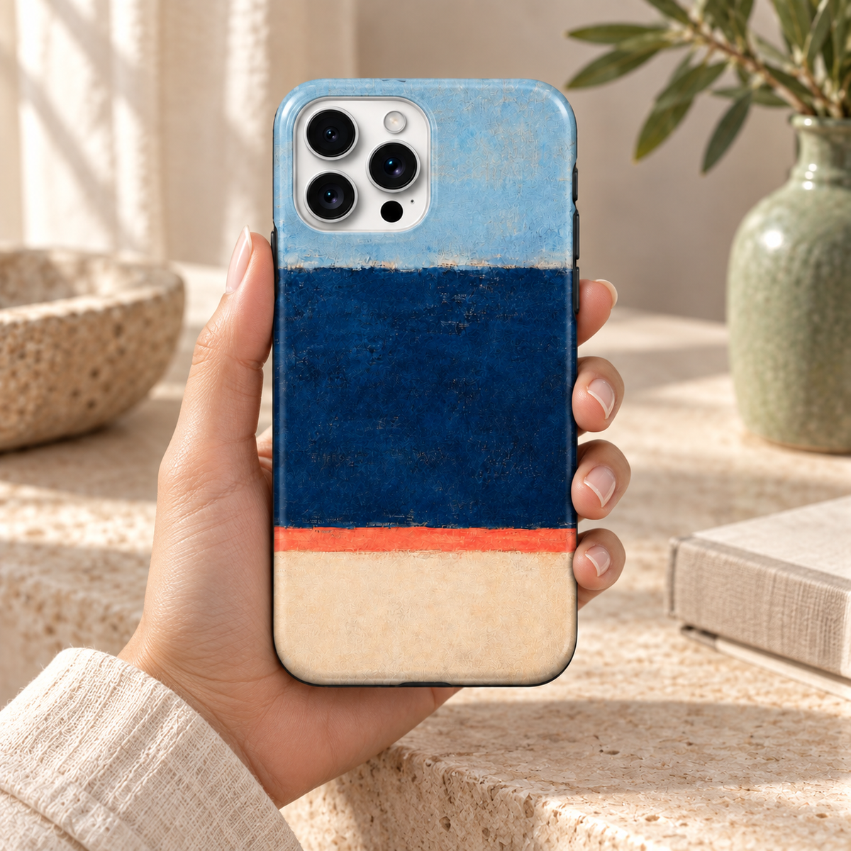 Coque Bleu profond tenue en main, motif abstrait bleu ciel, marine, corail et crème, dans un intérieur naturel.
