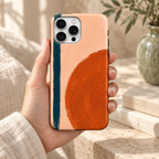 Coque Géométrie orange tenue en main, grand cercle orange et trait bleu pétrole sur fond pêche, décor crème naturel.
