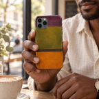 Coque Olive & Orange tenue en main dans un café, avec son motif abstrait imprimé.