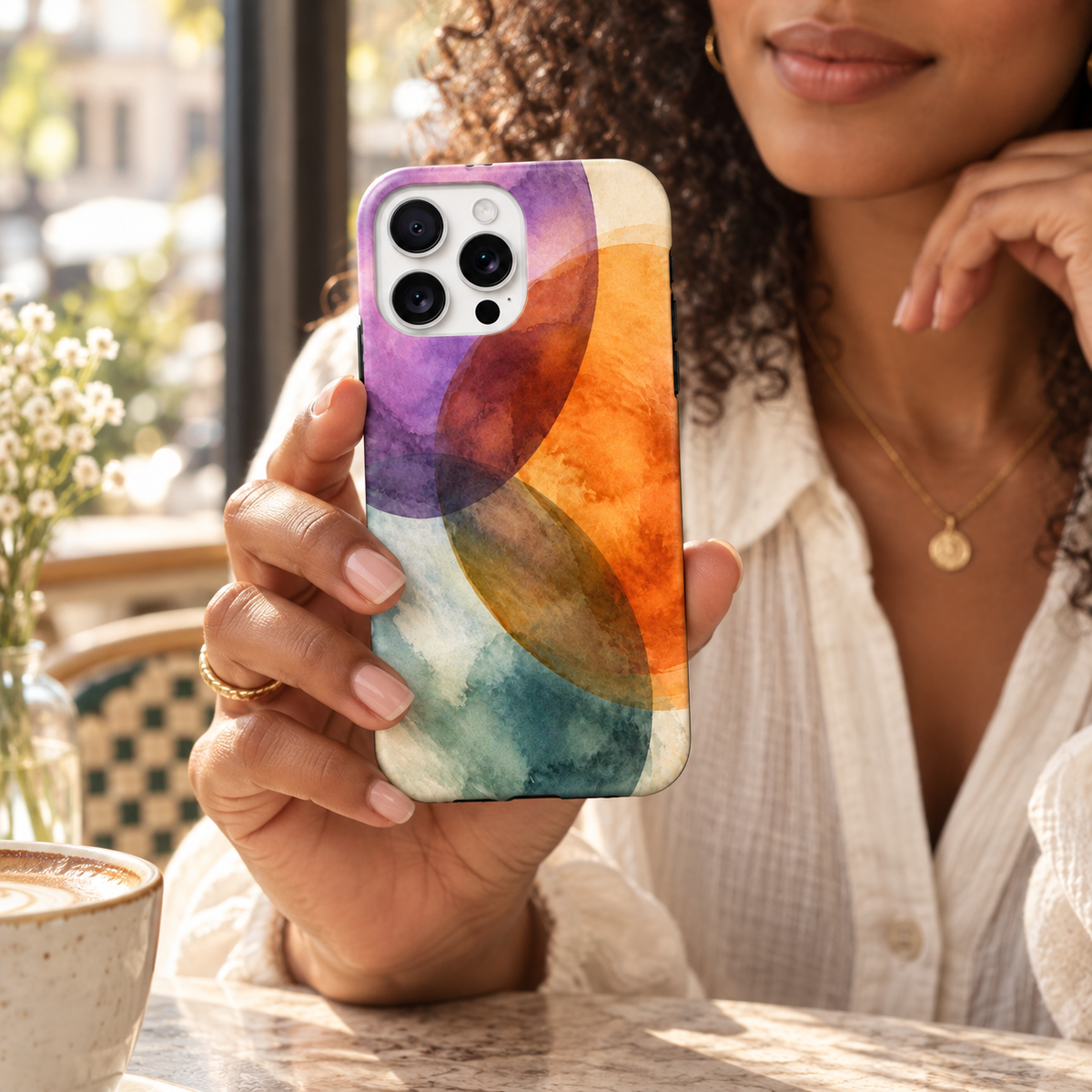 Coque Aquarelle vibrante tenue en main dans un café, avec son motif abstrait imprimé.