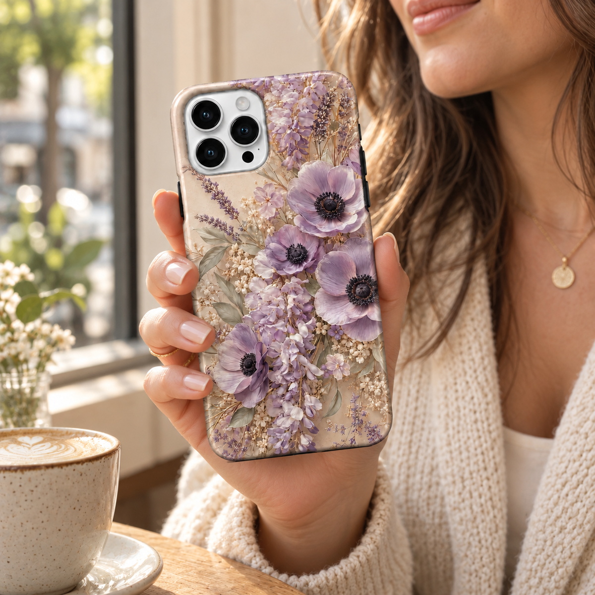 Coque Anémones lavande à motif floral imprimé, tenue en main près d’une fenêtre.